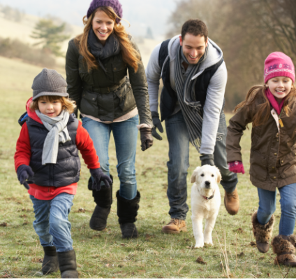 Family of four running outside with a white dog