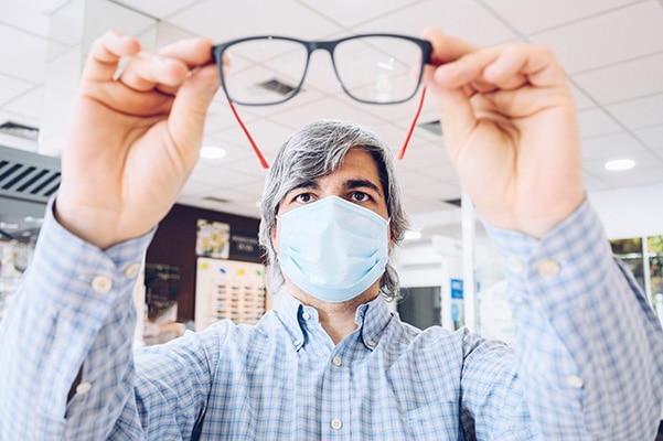 Man wearing mask, inspecting a pair of glasses