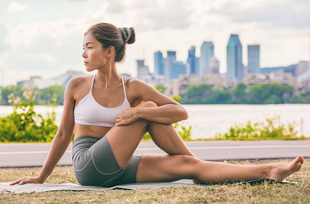 Woman stretching on a yoga mat outside, city skyline in the background
