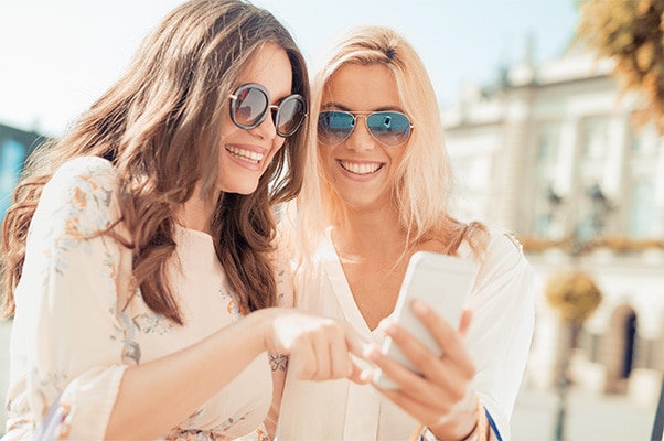 Two women in sunglasses smiling as they look at a cellphone