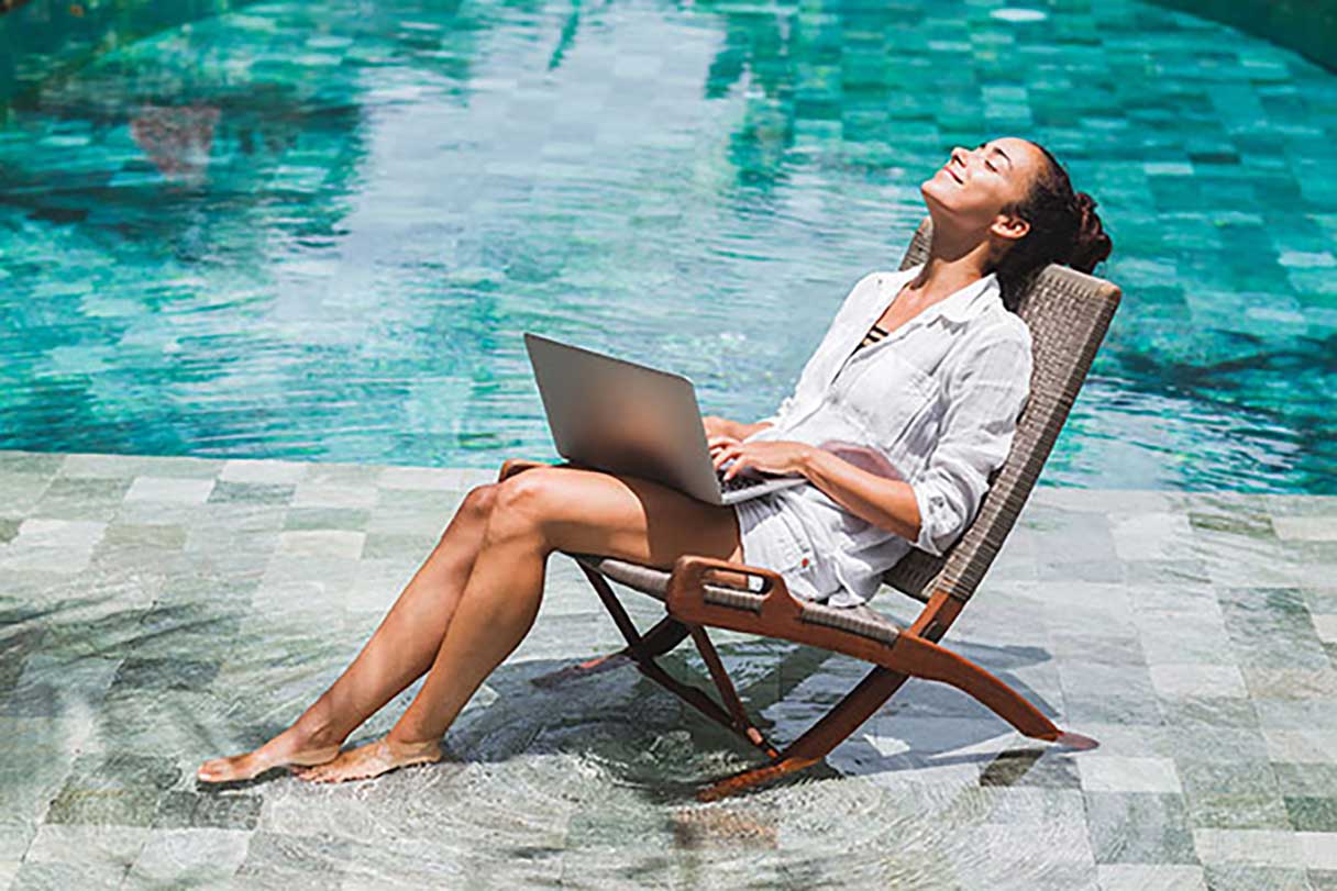 Woman working on laptop with head back, eyes closed, and feet in the pool