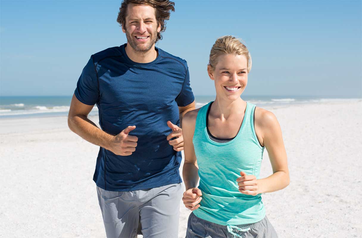 Man and woman smiling as they run on a beach