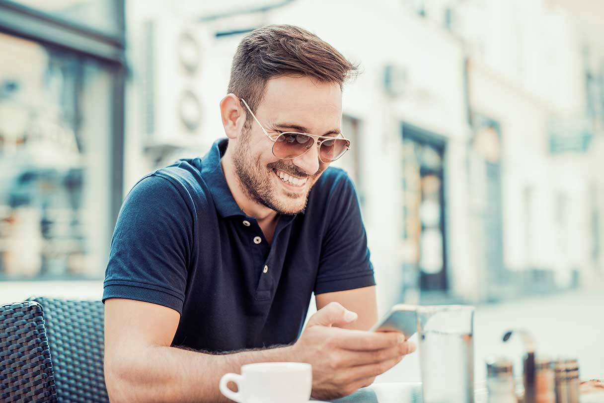 Man in sunglasses, smiling while he looks at his phone