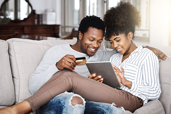 Man and woman sitting on couch, smiling, while they pay via credit card on a tablet