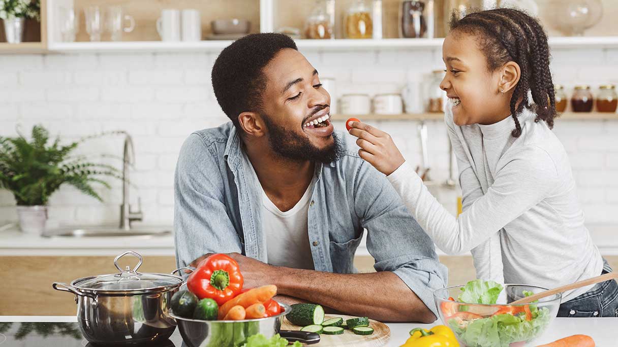 Girl feeding her dad a piece of food while they prepare meal together