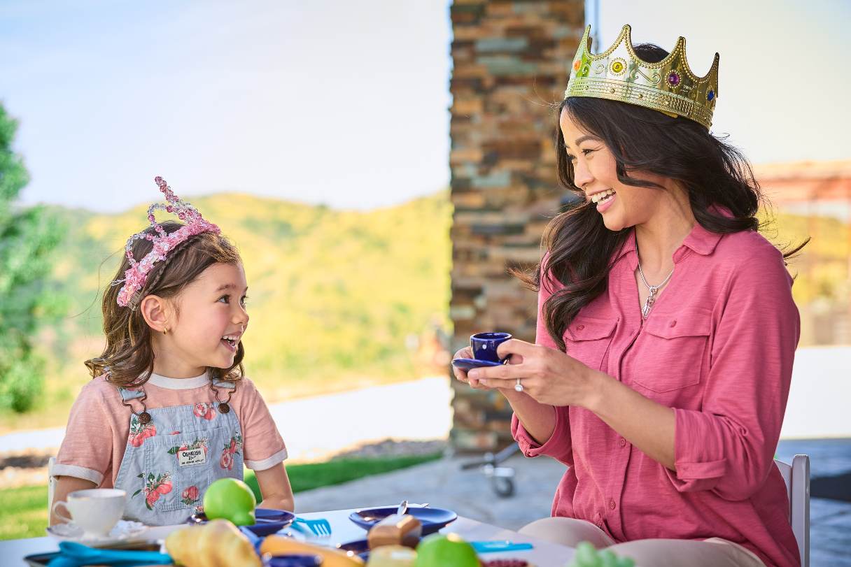 Woman having tea party with young girl, both wearing crowns