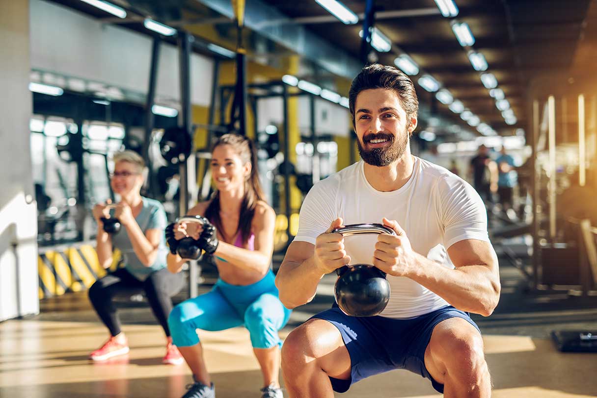 Three people working out in a gym with kettle bells