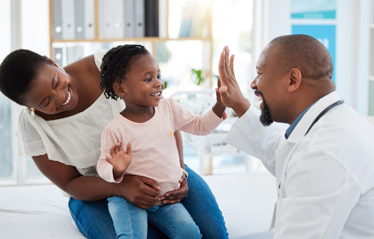 Doctor high-fiving little girl sitting in woman's lap