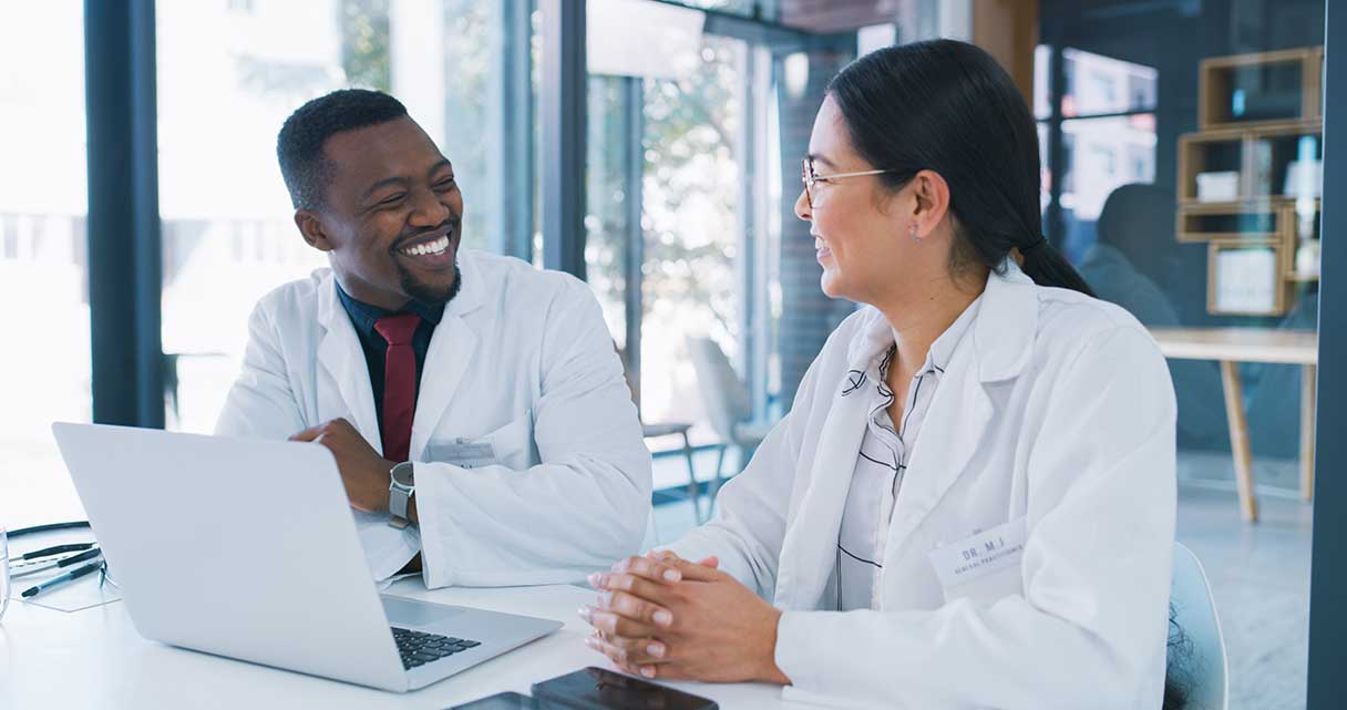 Two people in lab coats smiling at each other