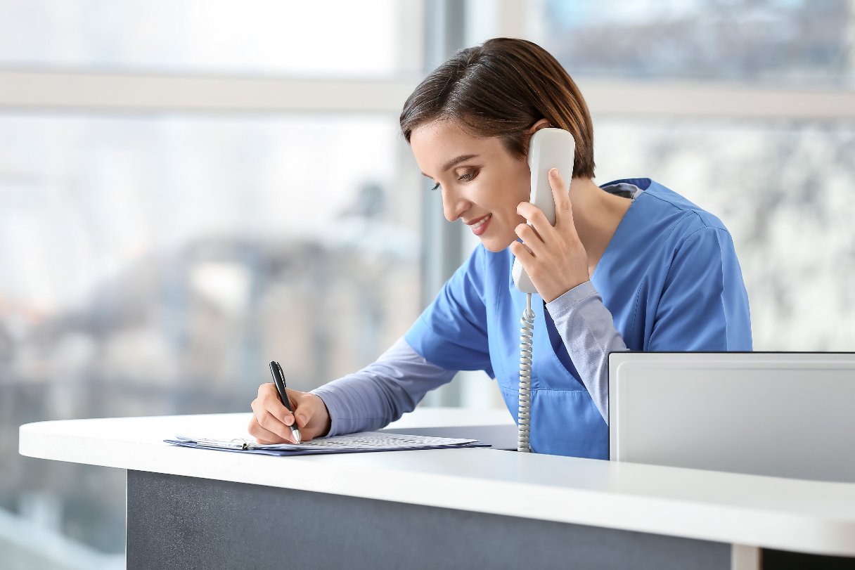 Receptionist wearing scrubs on phone at front desk